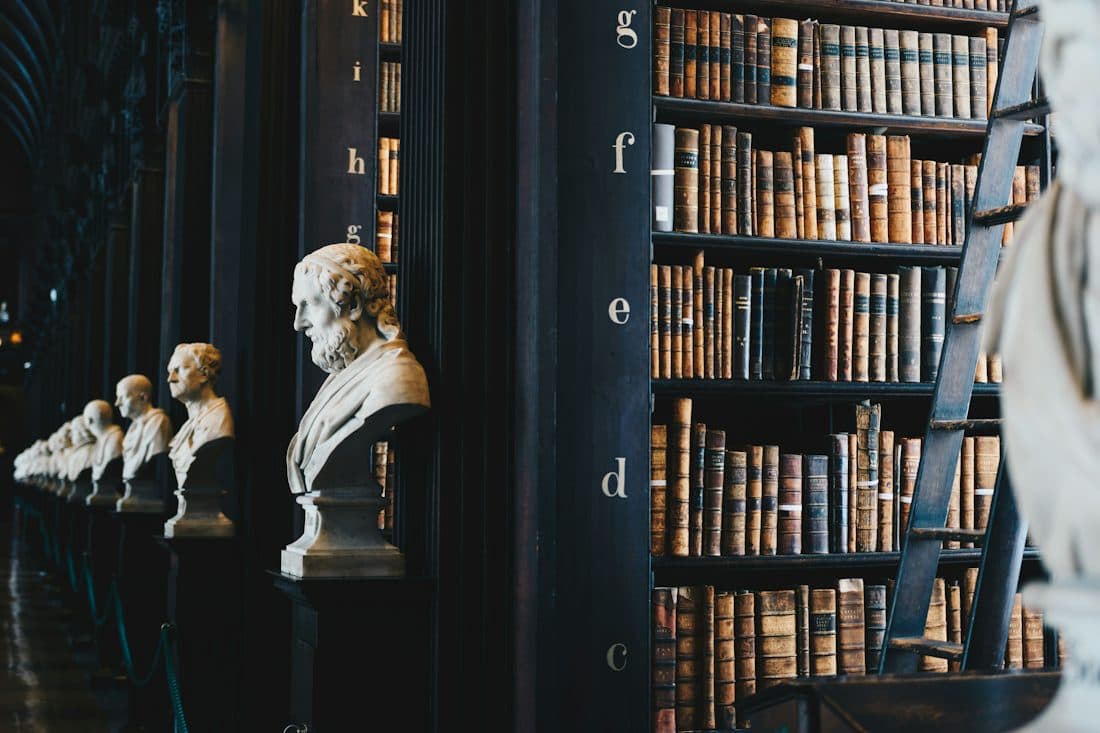 Biblioteca antiga com estantes de livros e bustos de mármore